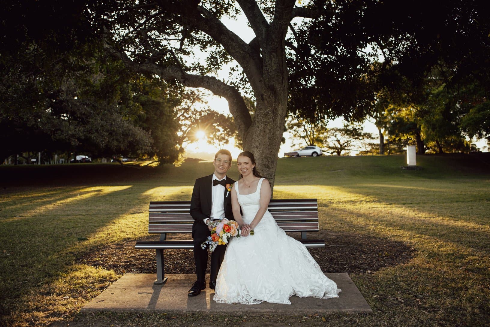 A photo of Helen and I sitting on a bench on our wedding day in a nice suit and dress in New Farm Park