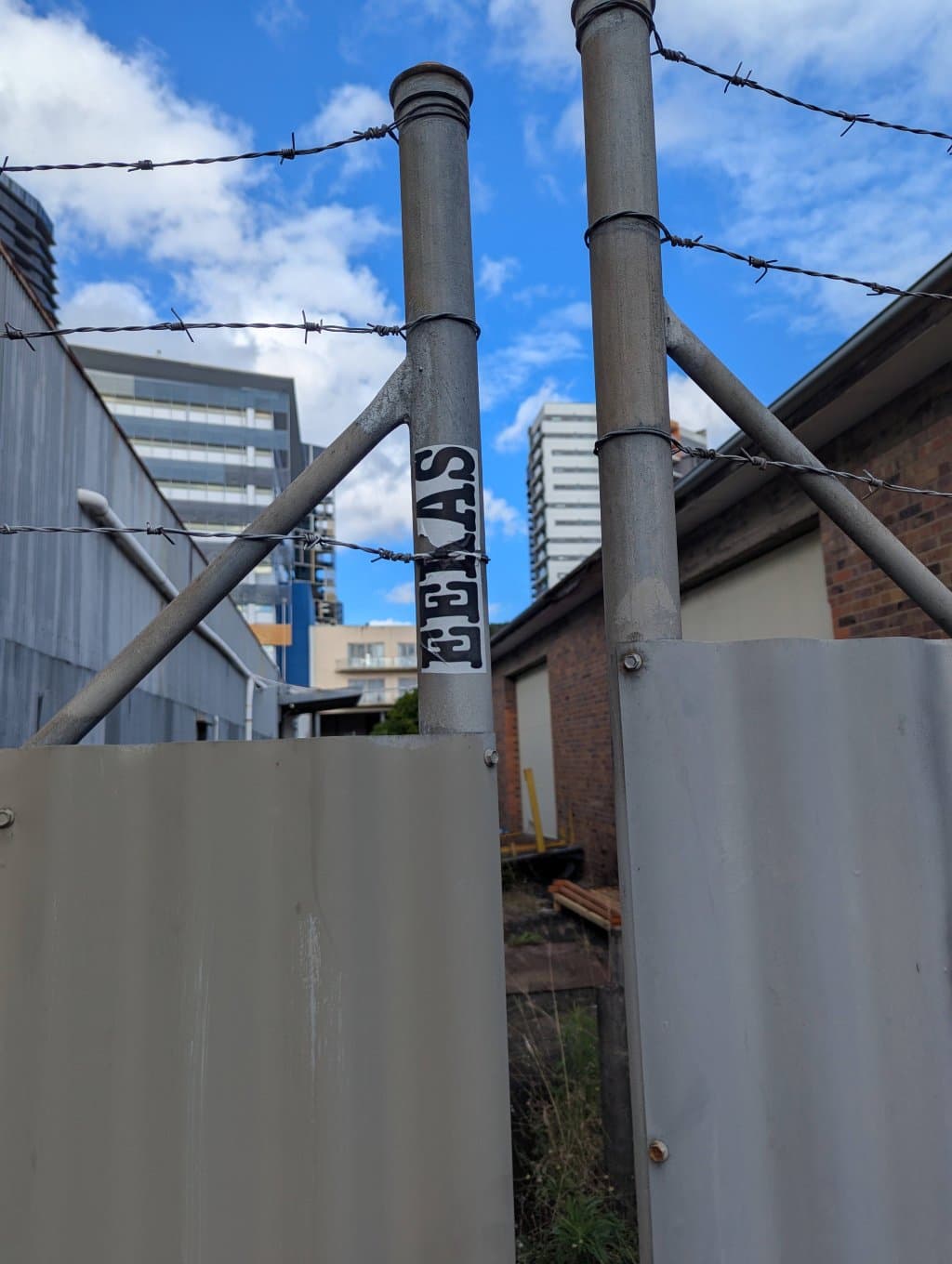 Another Eekas sticker on a pole, with the skyling of South Brisbane in the background.